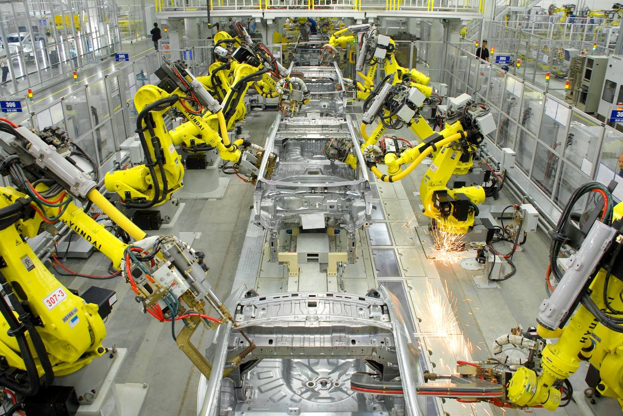 Factory floor digital signage screens showing real-time production metrics and safety alerts at an automotive manufacturing assembly line