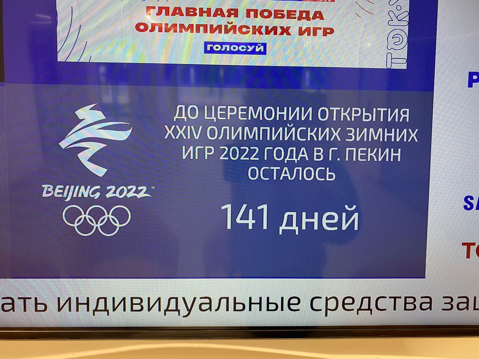 Large-format LED video wall at the Olympic Committee building showing real-time sports results, medal counts, and upcoming competition schedules