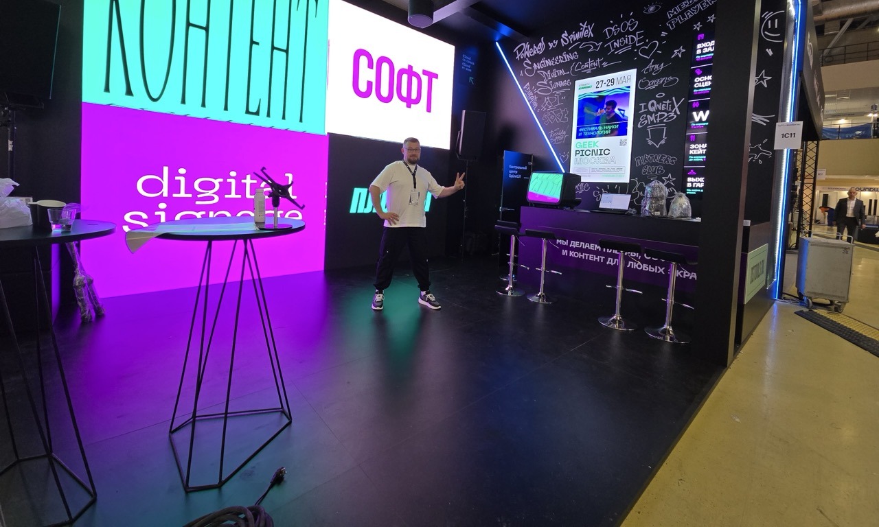 Technology exhibition booth with SpinetiX-powered digital screens displaying interactive product demonstrations, company information, and demo content